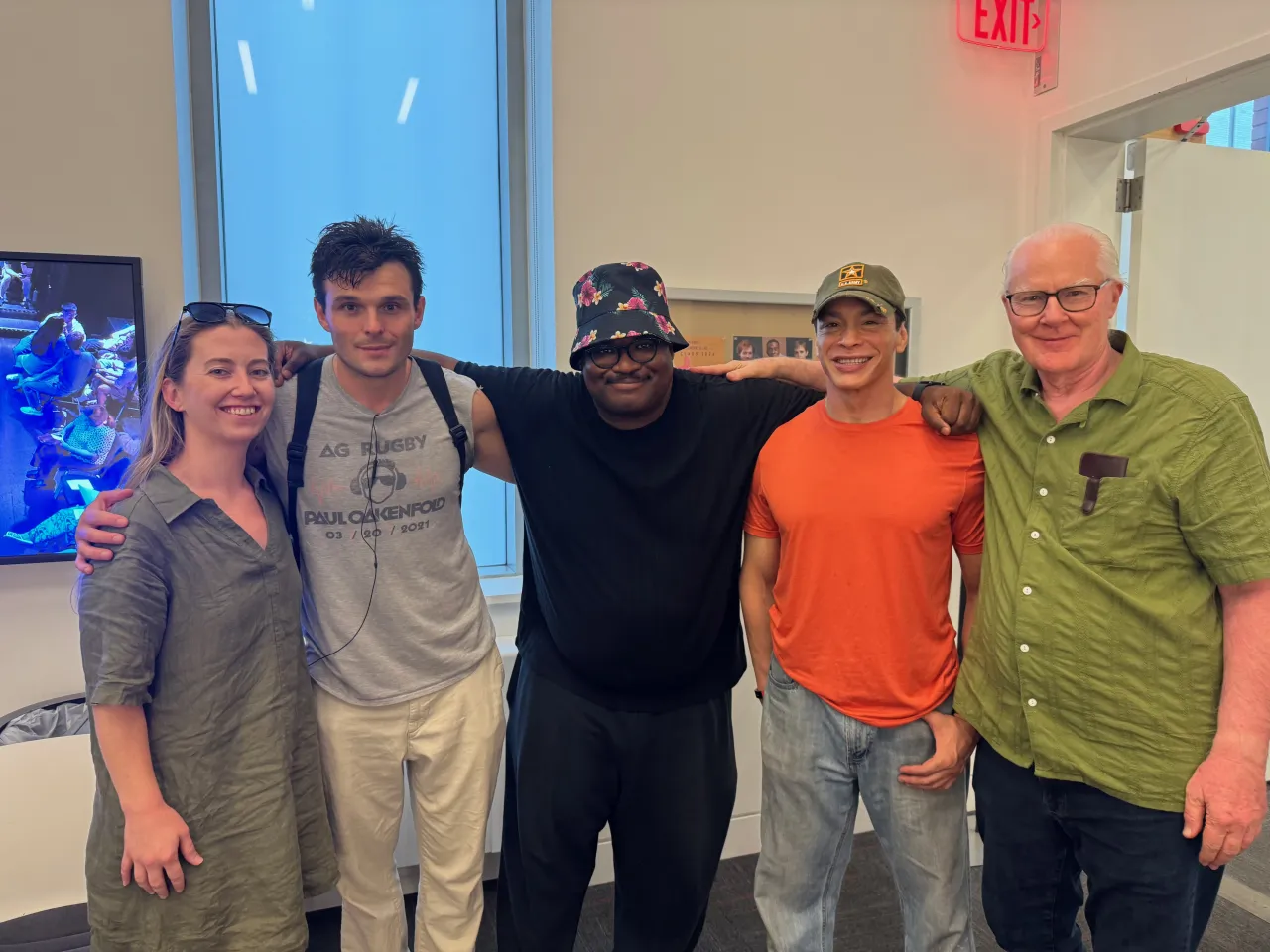 Five members of the A WALL company standing together, arms around each other, in the theatre lobby.