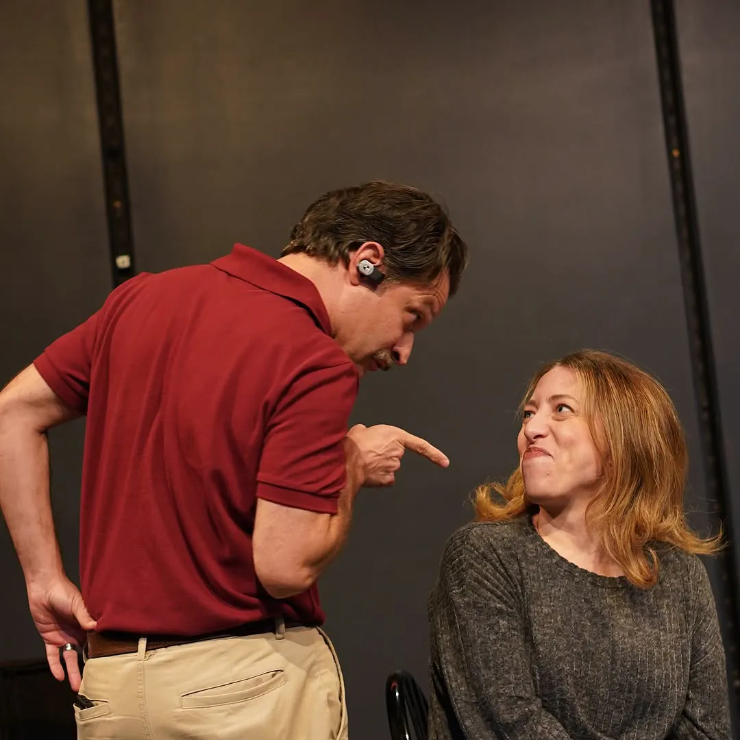 A man in a red polo leans down, pointing, at a seated woman.