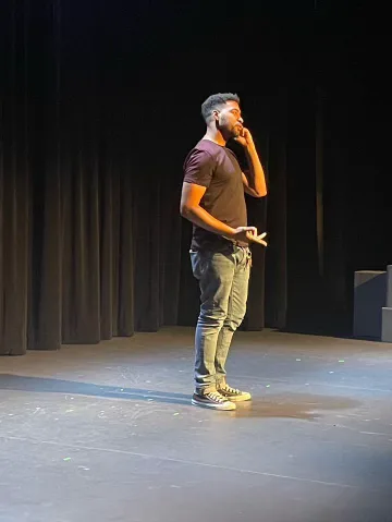 An actor stands alone on stage holding a phone to his ear.